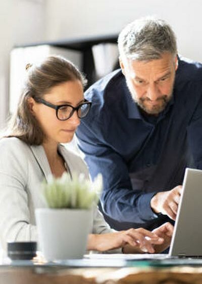 Image d'un homme montrant quelque à une femme sur ordinateur, illustrant le service informatique d'accompagnement proposé par Inibar Services.