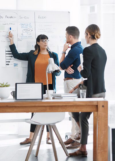 Photo d'une équipe en réunion devant un tableau blanc, illustrant le service informatique de gestion de projet proposé par Inibar Services.